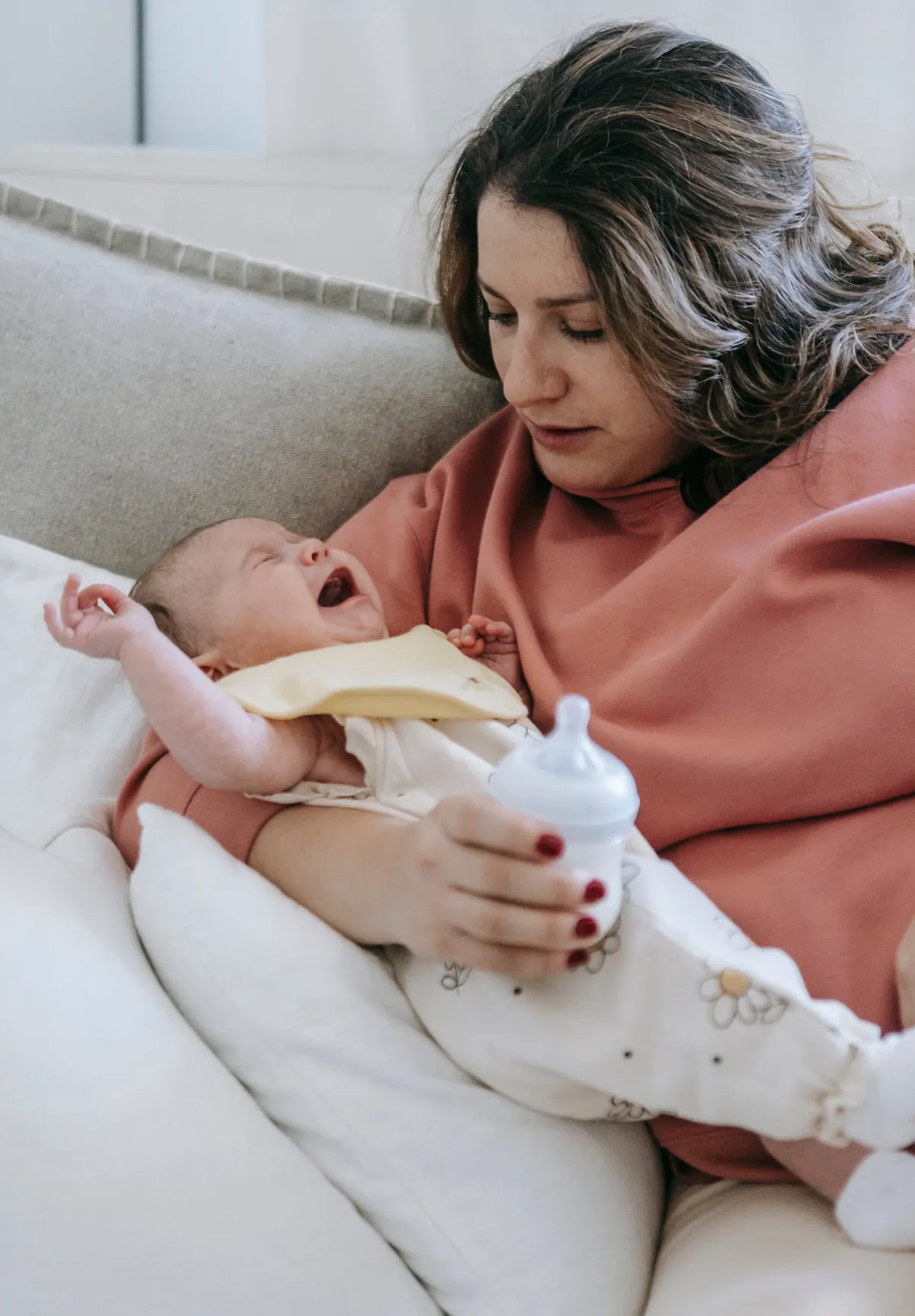Stressed mother holding crying baby showing bottle aversion during feeding attempt