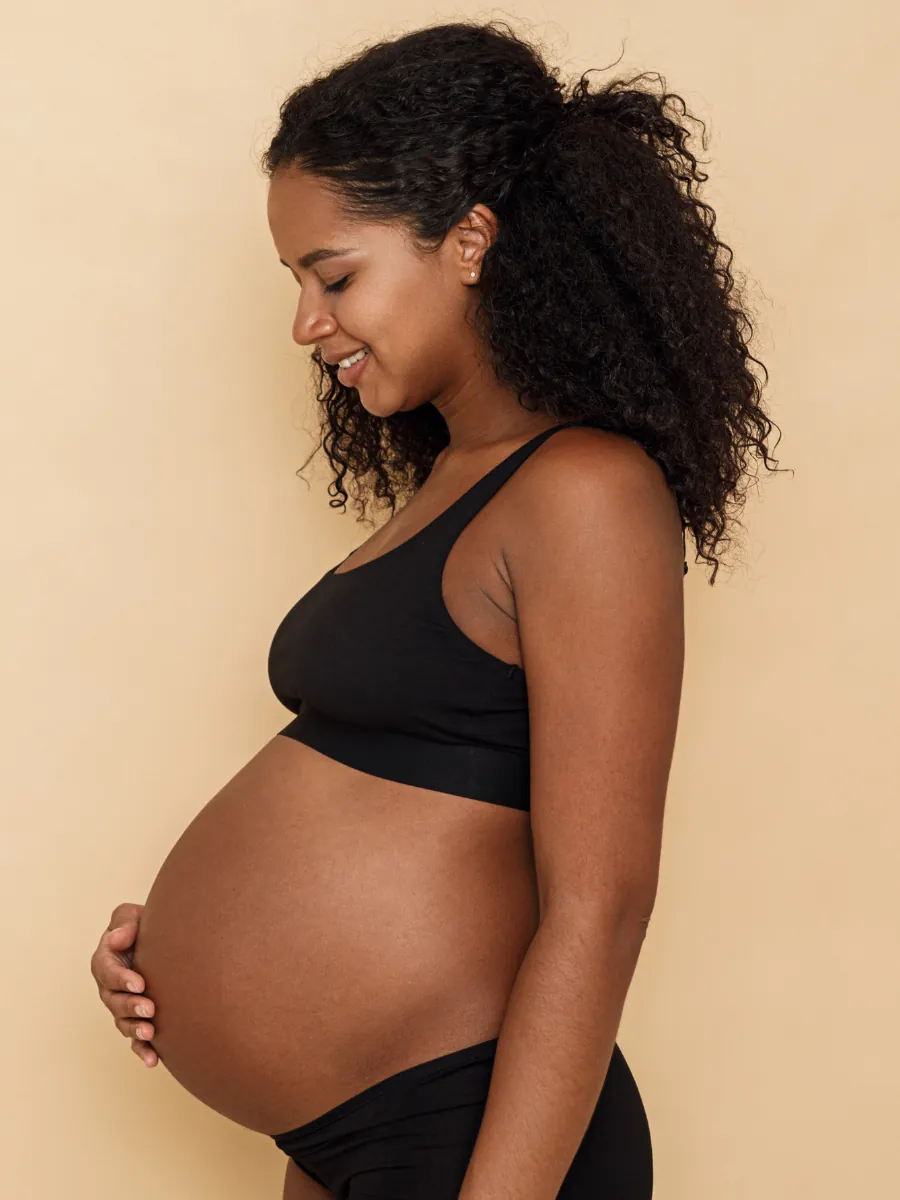Pregnant woman smiling and holding her bump, preparing for breastfeeding and antenatal support